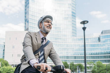 Happy businessman riding electric push scooter in front of office buildings - MEUF05842