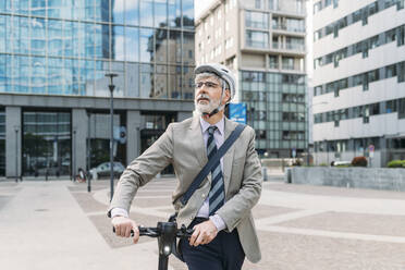 Geschäftsmann zu Fuß mit Elektro-Scooter vor einem modernen Bürogebäude - MEUF05844