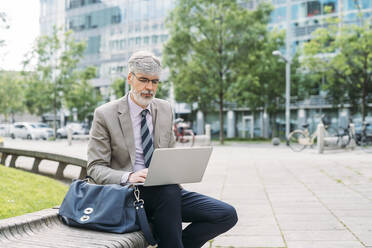 Freelancer working on laptop sitting on seat - MEUF05852