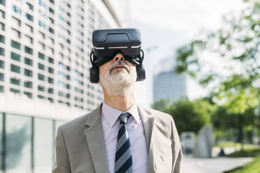 Geschäftsmann mit Virtual-Reality-Simulator vor einem Gebäude stehend - MEUF05857