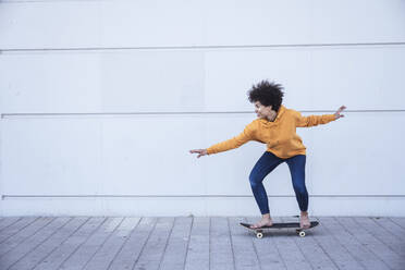 Frau auf dem Skateboard vor einer Mauer - UUF26210