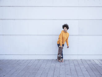 Frau mit Skateboard vor einer Wand stehend - UUF26211