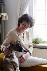 Senior woman stroking dog while sitting at home - MASF29719