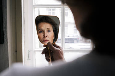 Spiegelung einer besorgten älteren Frau im Ruhestand mit Falten auf einem Handspiegel zu Hause - MASF29748