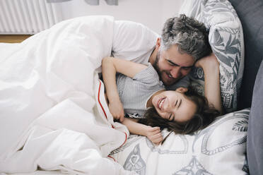 Cheerful daughter and father lying on bed at home - MASF29755