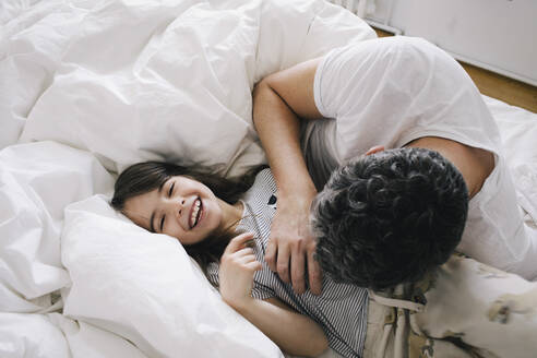 Playful father playing with daughter lying on bed at home - MASF29757