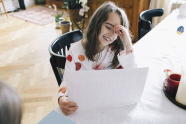 Happy girl with paper sitting at dining table - MASF29763