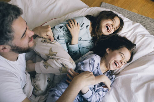 Glücklicher Vater mit verspielten Töchtern auf dem Bett zu Hause - MASF29772