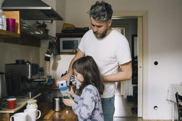 Vater und Tochter gießen Milch in einen Behälter am Küchentisch - MASF29780