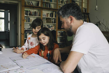 Zwillingsmädchen machen Hausaufgaben, während sie bei ihrem Vater am Tisch sitzen - MASF29789