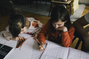 Mädchen macht Hausaufgaben, während ihre Schwester am Tisch zeichnet - MASF29790