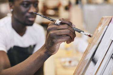 Junger Mann malt mit Pinsel auf Leinwand im Kunstunterricht - MASF29812