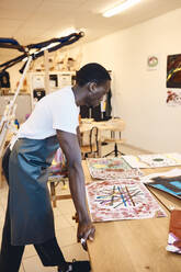 Seitenansicht eines jungen Mannes, der ein Bild auf einem Tisch im Kunstunterricht betrachtet - MASF29835