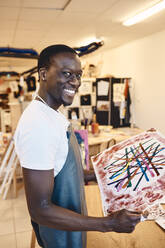 Porträt eines glücklichen männlichen Künstlers, der ein Gemälde hält, während er im Kunstunterricht steht - MASF29836