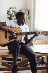 Junger Mann übt Gitarre, während er auf einem Tisch im Klassenzimmer sitzt - MASF29838