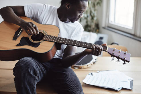 Junge Künstlerin mit Gitarre, die auf einem Tisch im Klassenzimmer sitzend eine Musiknote liest - MASF29841