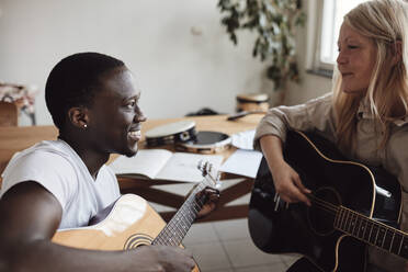 Lächelnder weiblicher reifer Lehrer, der einem jungen Mann im Klassenzimmer Gitarre beibringt - MASF29842