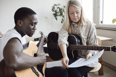 Junger männlicher Schüler, der mit einer Tutorin im Klassenzimmer Noten liest - MASF29844