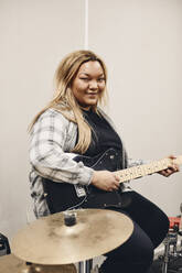 Porträt einer lächelnden jungen Frau, die im Klassenzimmer Gitarre übt - MASF29854