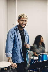 Portrait of smiling young artist holding microphone standing in classroom - MASF29855