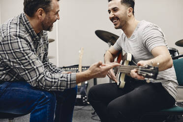 Glücklicher Mann übt Gitarre und sitzt mit einem Freund im Klassenzimmer - MASF29858