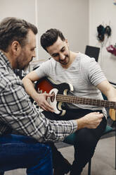 Älterer Mann unterrichtet Gitarrenschüler im Klassenzimmer sitzend - MASF29859