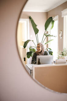 Reflexion einer lächelnden Freiberuflerin, die zu Hause am Laptop arbeitet - MASF29932