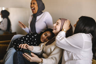 Junge Frauen, die lachend zu Hause auf dem Sofa sitzen - MASF29988