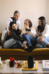 Glückliche junge Frauen lachen, während sie zusammen auf dem Sofa sitzen und sich zu Hause amüsieren - MASF29989