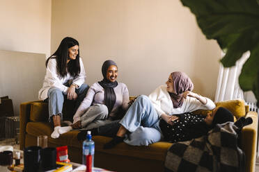 Smiling young women talking with each other while sitting on sofa in living room at home - MASF29991