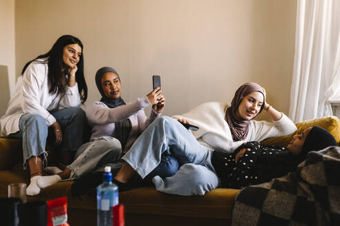 Junge Frauen im Gespräch mit Freunden, die zu Hause ein Selfie mit ihrem Handy machen - MASF29992