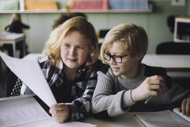 Freunde betrachten ein Dokument, während sie in der Schule im Klassenzimmer sitzen - MASF30004
