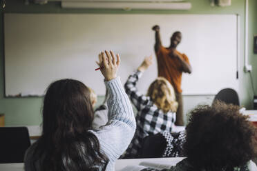 Rückansicht eines Mädchens, das die Hand hebt, während es mit Schülern im Klassenzimmer sitzt - MASF30008