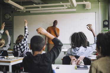 Rückansicht von Studenten verschiedener Rassen, die während einer Vorlesung im Klassenzimmer die Hände heben - MASF30009