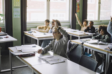 Junge mit erhobener Hand, der am Schreibtisch sitzt und an einer Vorlesung im Klassenzimmer teilnimmt - MASF30011
