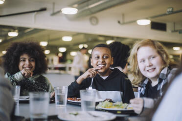 Lächelnde Schüler, die in der Mittagspause in der Cafeteria am Tisch sitzen und wegschauen - MASF30038