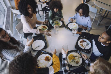 Hochformatige Ansicht von Schülern, die während der Mittagspause in der Cafeteria mit einem Lehrer am Tisch essen - MASF30044