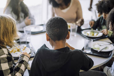 Rückansicht eines Jungen, der mit Freunden am Tisch in der Cafeteria sitzt - MASF30045