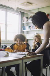 Students looking at book while teacher explaining in classroom - MASF30054