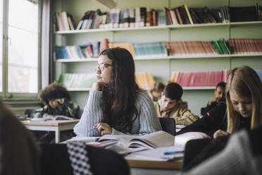 Mädchen mit Hand am Kinn sitzt am Schreibtisch während einer Prüfung im Klassenzimmer - MASF30068