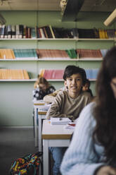 Schuljunge sitzt auf dem Schreibtisch im Klassenzimmer - MASF30069