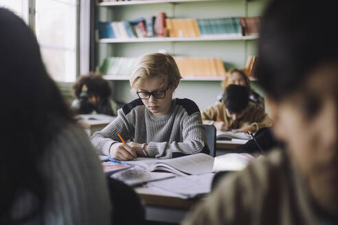 Ein Schüler schreibt während einer Prüfung im Klassenzimmer in ein Buch - MASF30074