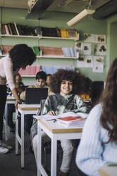 Smiling student with curly hair sitting at desk in classroom - MASF30080
