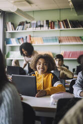 Lächelndes Mädchen mit Laptop am Schreibtisch im Klassenzimmer - MASF30083