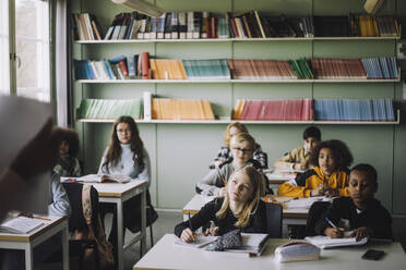 Unterschiedliche Schüler schreiben, während sie dem Lehrer während einer Vorlesung im Klassenzimmer zuhören - MASF30085