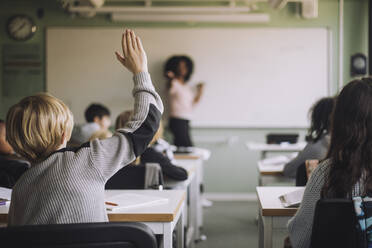 Rückansicht eines Schülers, der die Hand hebt, während der Lehrer im Klassenzimmer unterrichtet - MASF30091