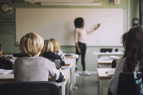 Rückansicht von Schülern, die am Schreibtisch sitzen, während der Lehrer im Klassenzimmer unterrichtet - MASF30092