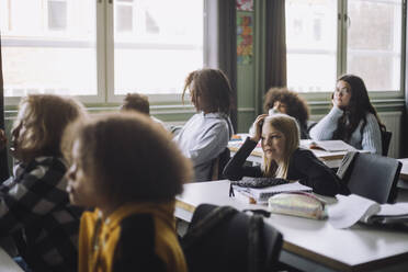 Gelangweiltes Mädchen, das sich auf den Ellbogen stützt, während es während einer Vorlesung im Klassenzimmer am Schreibtisch sitzt - MASF30095
