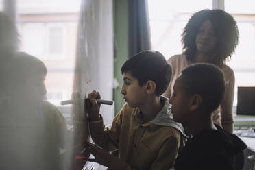 Boys doing mathematics on white board while teacher examining in classroom - MASF30098