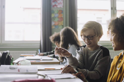 Lächelnde Freunde, die am Schreibtisch im Klassenzimmer sitzen und spielen - MASF30104